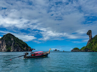 Fototapeta premium A traditional Thai long-tail boat is anchored in a tranquil bay, with iconic silhouette of Chicken Island in distance. Serene and beautiful seascape representing travel and holidays in Krabi, Thailand