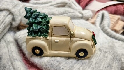 Delivery gift of a white Christmas car with a Christmas green tree, a toy for winter holidays on knitted warm blankets, thematic decor for children's parties, winter gift