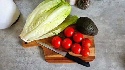 Proper nutrition at home, fresh vegetables and avocado, fresh salad on a wooden board with a knife with a black handle. Pepper seasonings and napkins on the kitchen table. kitchen interior, cooking 