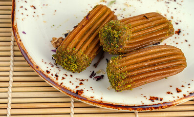 Close-up of three pieces of Turkish dessert tulumba topped with ground pistachio served on a rustic plate. Showcasing sweet syrup texture, delicious glaze and traditional pastry flavor.
