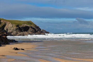 Beachside view with a rocky cliff on the left and waves in the distance in Polly Joke - Cornwall - UK