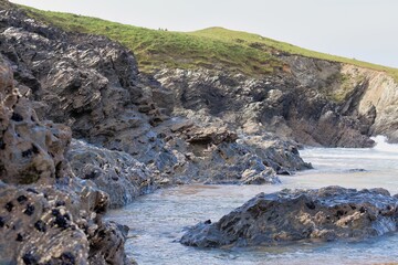 Coastal rocks meet the surf on a sunny day. A grassy bluff rises in the background in Polly Joke - Cornwall - UK