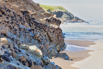 A rocky coastal scene with the tide rolling in. Rugged cliffs meet the sandy beach, with the ocean stretching to the horizon in Polly Joke - Cornwall - UK