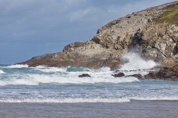 Rocky coastline with waves. Waves crash on rocks under a cliff against a blue sky in Polly Joke - Cornwall - UK