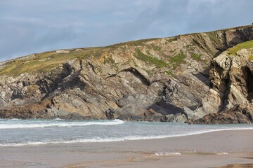 Rocky coastline with exposed layers of stone meets a sandy beach in Polly Joke - Cornwall - UK