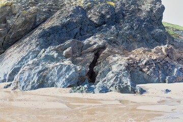 a rocky coastal landscape. The focus is on the rock formation with a dark crack, contrasting with the sandy beach below in Polly Joke - Cornwall - UK