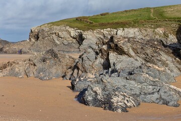 grey rocks on a sandy beach at the foot of a green hillside under a cloudy sky in Polly Joke - Cornwall - UK