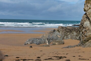 Sandy beach with rocky outcroppings meets ocean. White-capped waves roll to shore under a cloudy sky in Polly Joke - Cornwall - UK