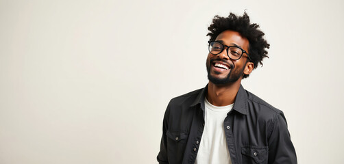 Smiling young black man with glasses, afro hairstyle. Wears casual outfit with white t-shirt, black jacket. Man beard, looks happy. Isolated on plain background. Panoramic studio shot of joyful male