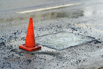 Road repair work on city road with traffic cones, laying fresh asphalt over potholes to restore the...