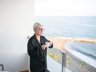Woman enjoying coffee on balcony overlooking serene ocean view