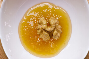 Peeled walnut soaked in a vessel with natural honey, macro shot.