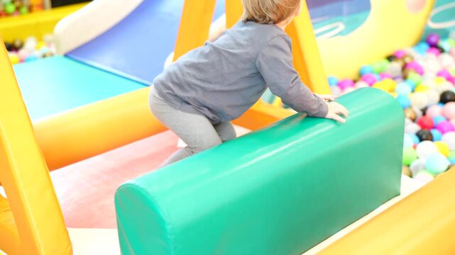 Small child exploring soft indoor obstacle elements while climbing and moving across padded surfaces inside a colorful recreational play area