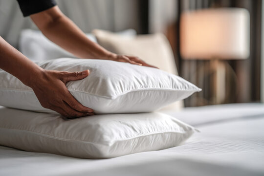 Close-up of a maid's hands fluffing a pillow in a hotel room