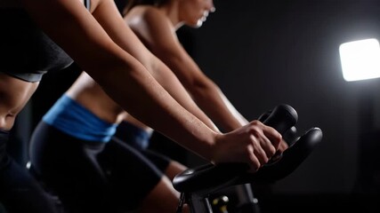 Closeup of peoples hands gripping handlebars while riding stationary bikes in a dimly lit fitness class - Powered by Adobe