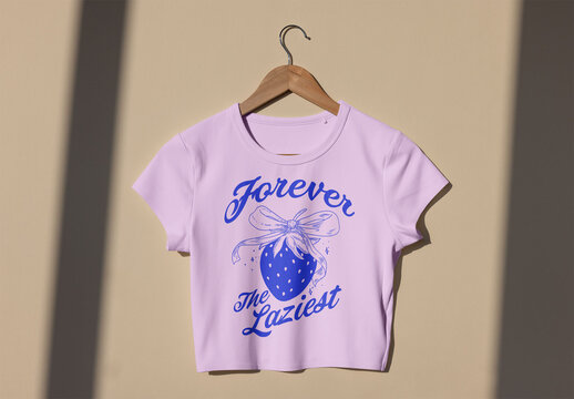 Mockup of T-shirt displayed on a wooden hanger against a beige wall