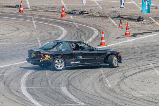 Outdoor racing track, Kyiv Car Drifting Festival, BMW sports car mid-drift, black vehicle with number and sponsor, orange cones for guidance, bright daylight - Kyiv, Ukraine 06-15-2025