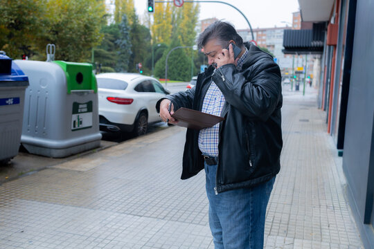 Mature man talking on phone checking wallet walking street