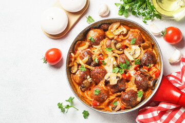 Meatballs with mushrooms in tomato sauce in a frying pan.