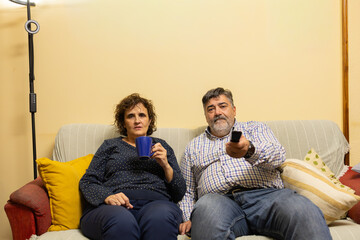 Middle aged couple relaxing on couch watching television