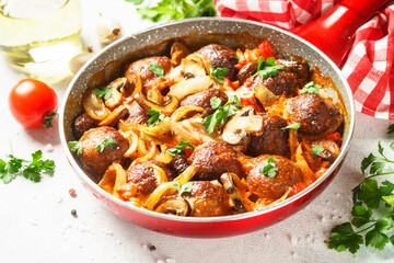 Meatballs with mushrooms in tomato sauce in a frying pan.