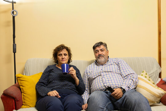Bored middle-aged couple relaxing watching television at home