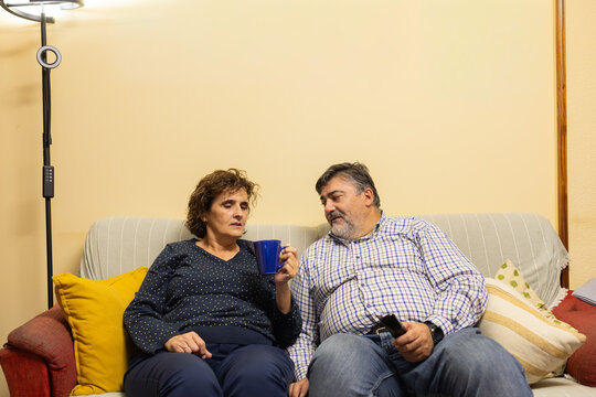 Middle-aged couple talking relaxing on home sofa