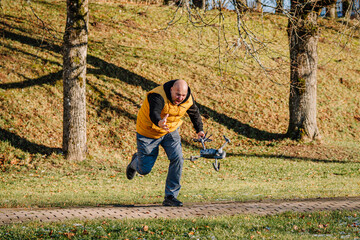 Pilot in yellow jacket runs to save falling drone in park, showcasing urgency and determination in outdoor technology mishap scenario