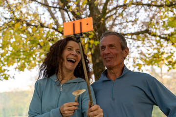 Happy couple taking a selfie with a selfie stick and mushroom in an autumn park