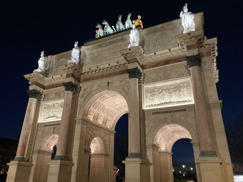 Arc de Triomphe du Carrousel in Paris bei Nacht, beleuchtet mit detaillierten Reliefs, S&auml;ulen und Quadriga-Skulptur vor dunkelblauem Himmel