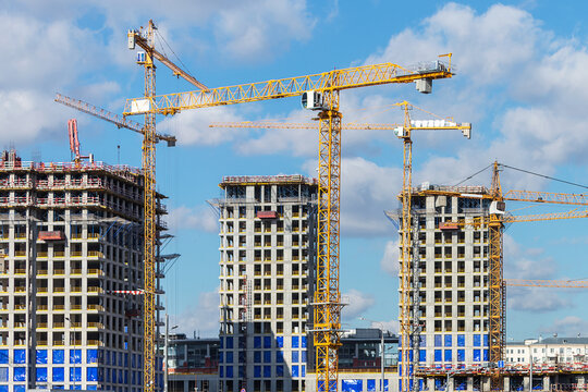 Multiple yellow cranes tower over high-rise buildings under construction against  bright blue sky. A dynamic scene of urban development and modern engineering in progress - Powered by Adobe