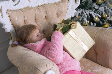 a little girl in a pink sweater is sitting in a chair and being handed a large box wrapped in Christmas paper