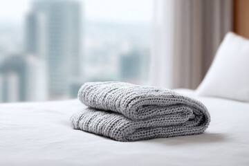 Cozy knitted blanket folded on a bed in a bright, modern bedroom with a blurred city view. Represents comfort, relaxation, and simple luxury. Perfect for lifestyle and home decor.