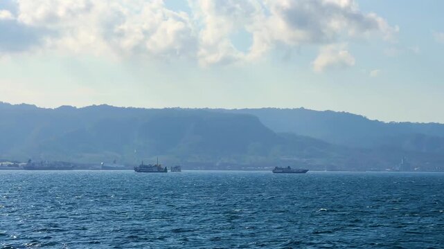 Bali, Indonesia - August 27, 2025: Car and passenger ferries cross the Bali Strait from Gilimanuk Harbor to Ketapang Harbor on the island of Java. View of the strait from the ferry deck. 4K