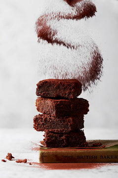 Stacked Chocolate Brownies with Falling Cocoa Powder on Light Background