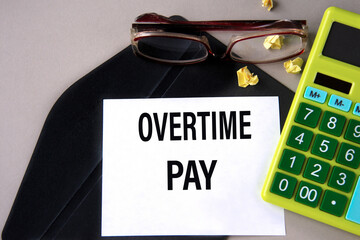 OVERTIME PAY - words on a white sheet on a black envelope with a calculator and glasses