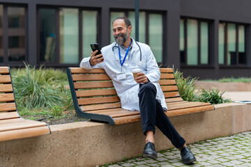 Doctor smiling, using smartphone during coffee break