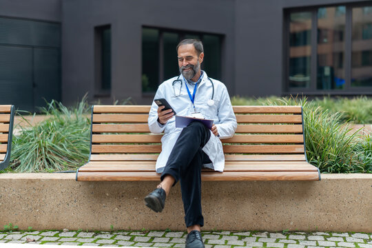 Male doctor relaxing outdoors checking communication on smartphone