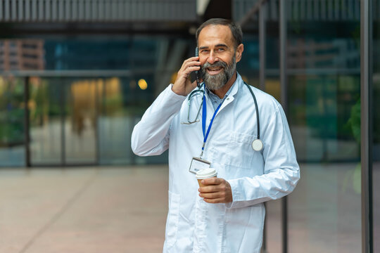 Happy mature doctor talking on cell phone outside hospital