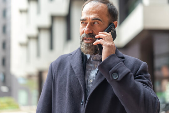 Mature man talking on smartphone discussing business outdoors - Powered by Adobe