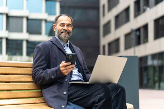 Senior businessman multitasking with smartphone and laptop outside office