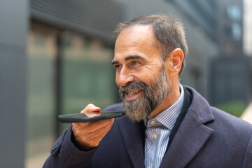 Mature businessman recording voice message on smartphone