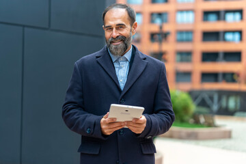 Confident mature businessman using tablet smiling outdoors