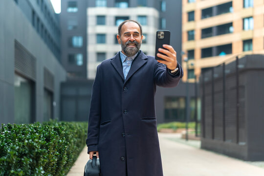 Mature man smiling taking selfie with smartphone in urban setting