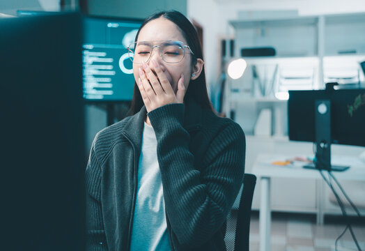 Young female programmer yawning while code and deadlines at her desk. The concept of working overtime