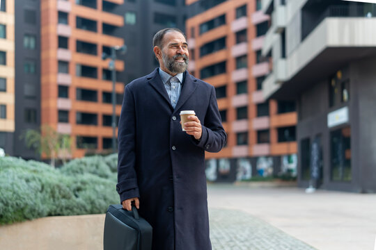 Mature businessman smiling walking with coffee cup in urban setting