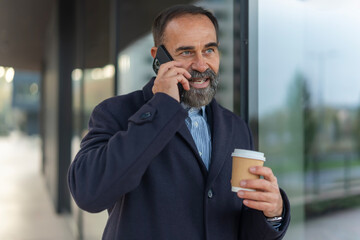 Confident businessman talking on smartphone holding coffee cup