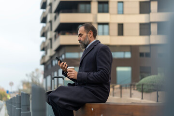 Mature businessman checking smartphone and enjoying coffee during travel