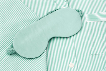 Top view mint color sleep eye mask on folded striped green pajama, close up textured photo. Minimal style, cozy, and comfort Fashion sleepwear. Self-care, wellness, calm lifestyle, home aesthetics