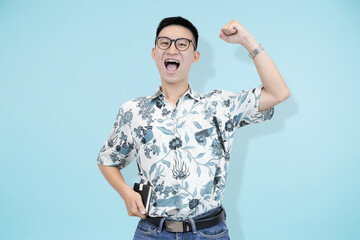 Naklejka premium A cheerful and confident young Asian man and batik shirt, standing confidently in blue studio background